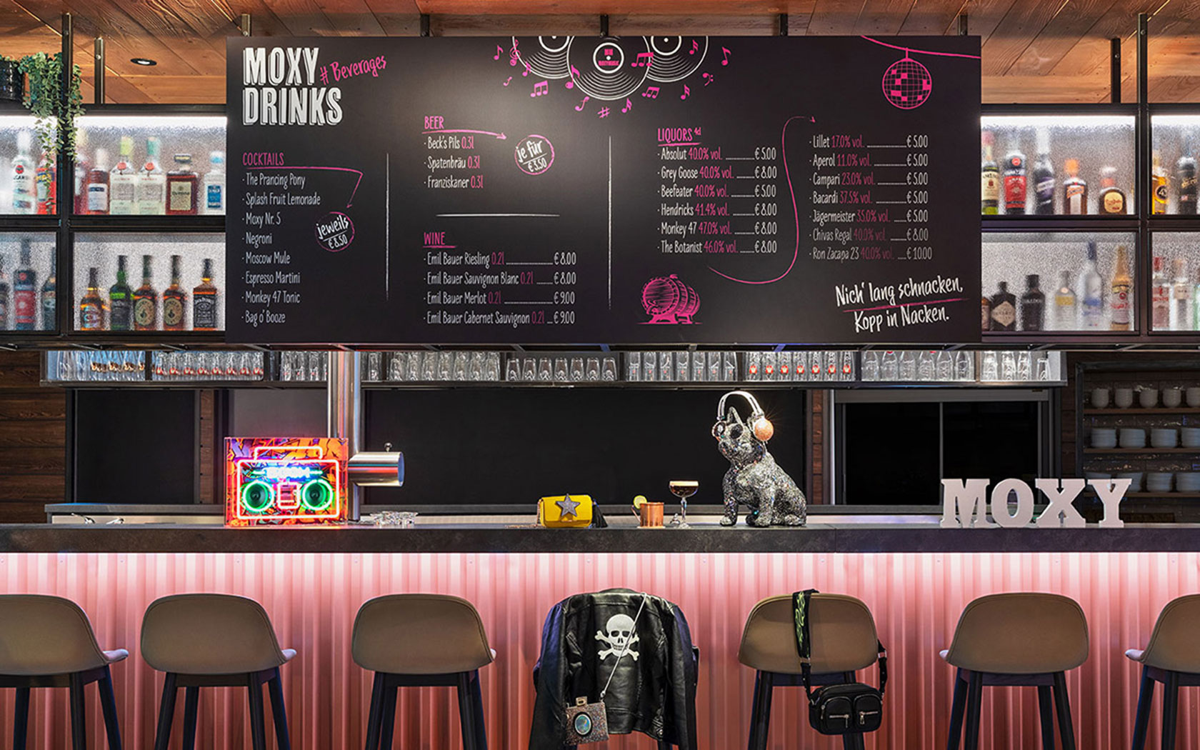Moderne Bar mit Barhockern, Dekoration, Tafel mit Getränkeangebot und Flaschen im Hinzergrund für Moxy Hotels.