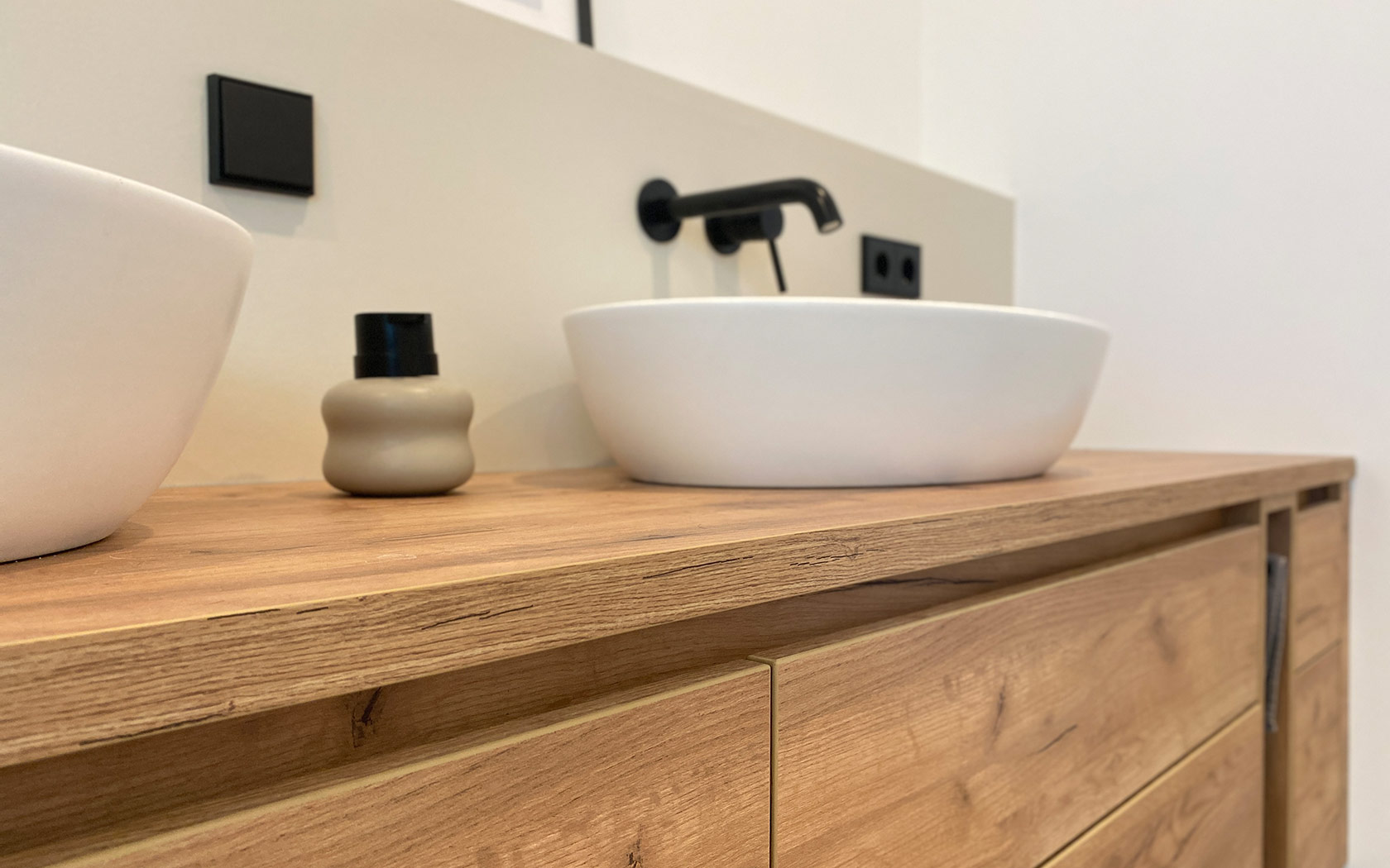 2 Weiße Keramikwaschbecken mit schwarzer Amatur auf einem Holzsideboard